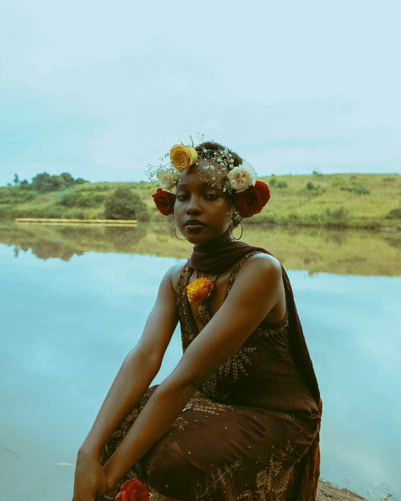 A woman sitting on a rock beside still water.