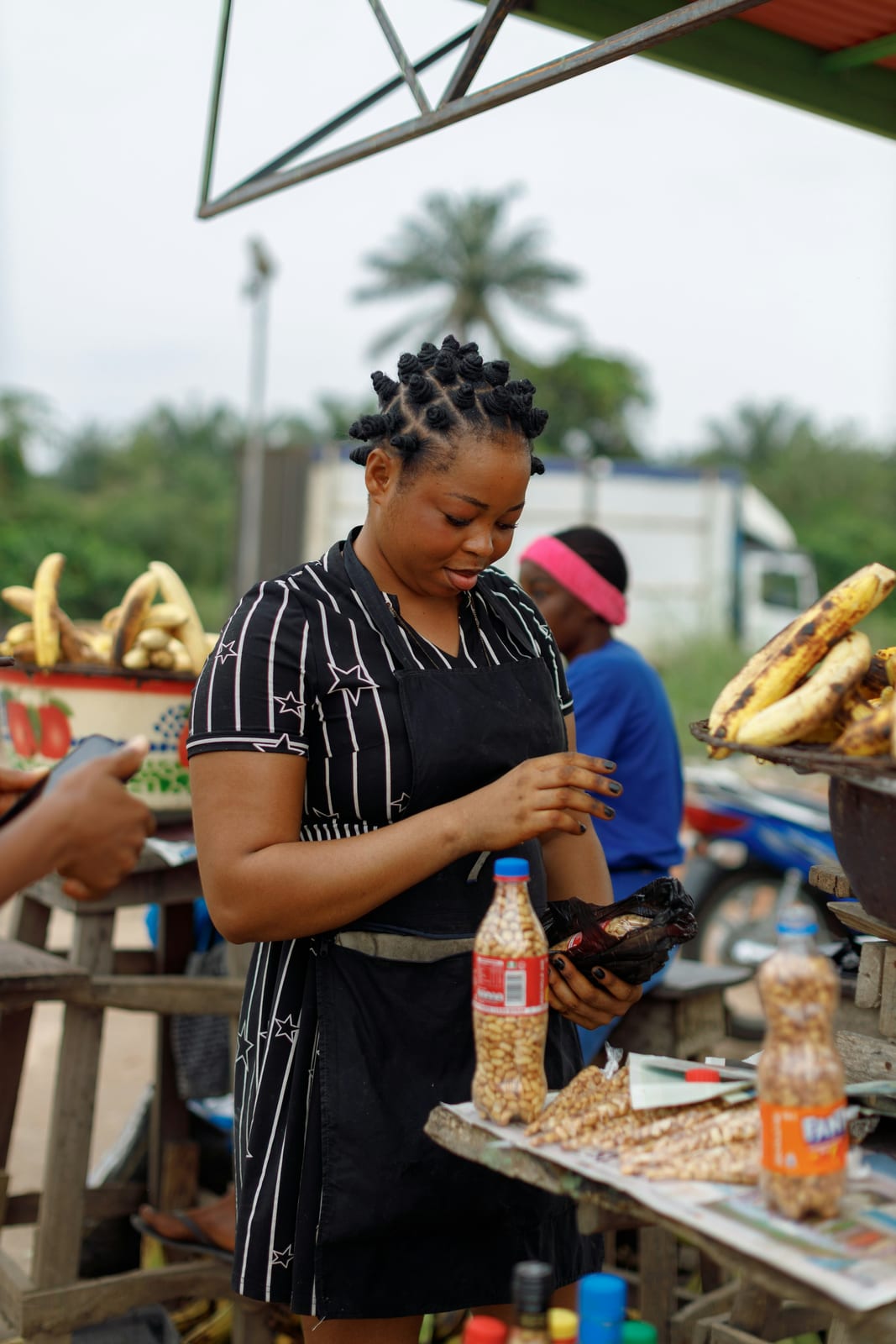 A woman at her roadside food stall, roasted plantain beside her.