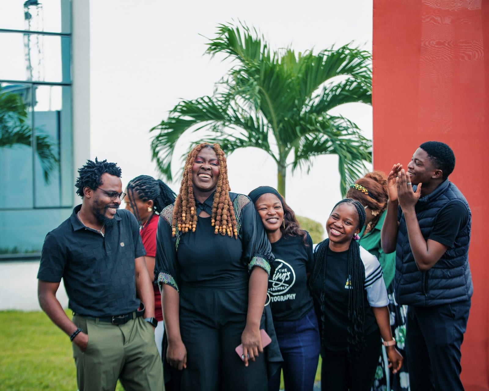A group of friends laughing together outdoors, under palm trees.