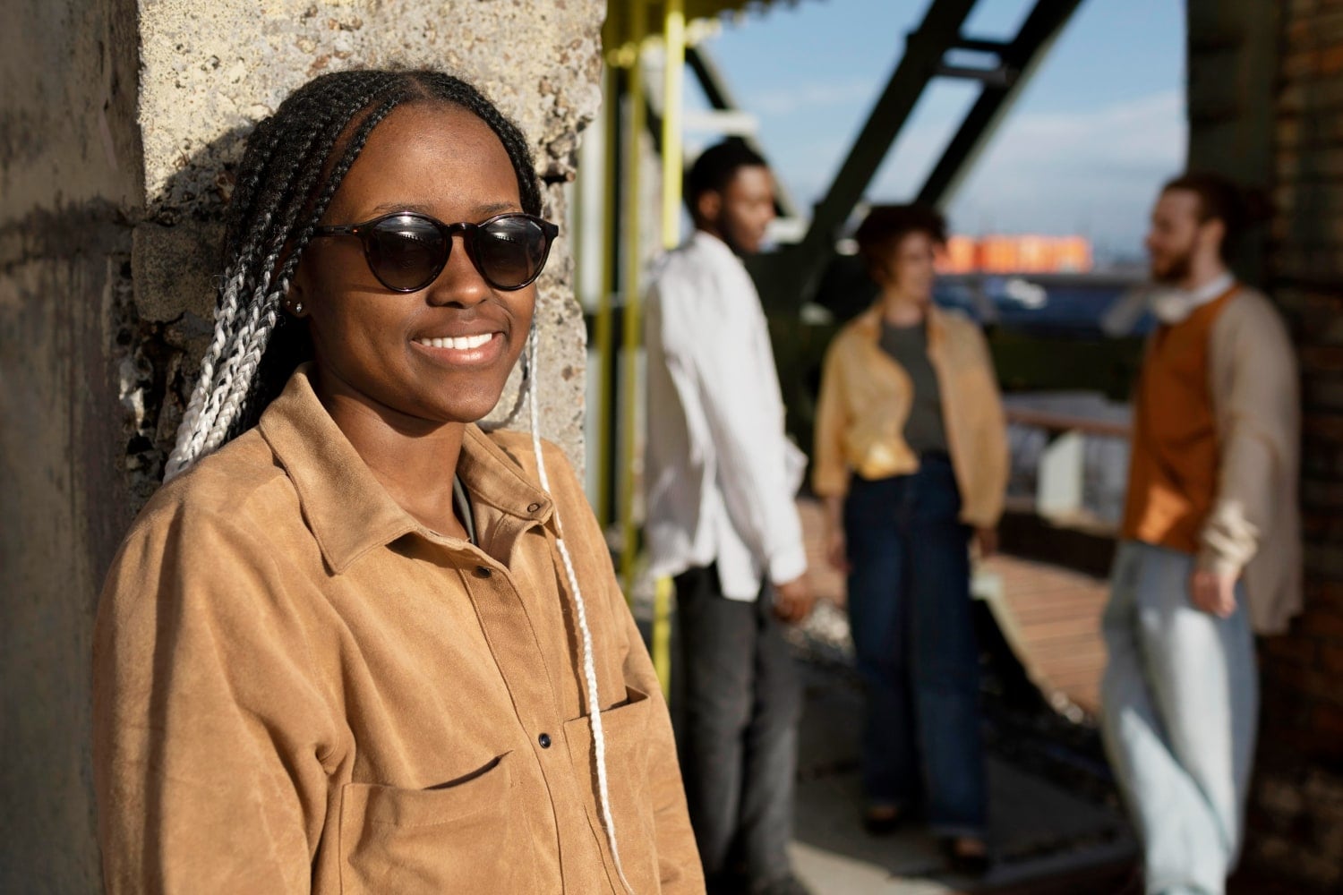 A woman in sunglasses smiles on a city street, friends talking behind her.
